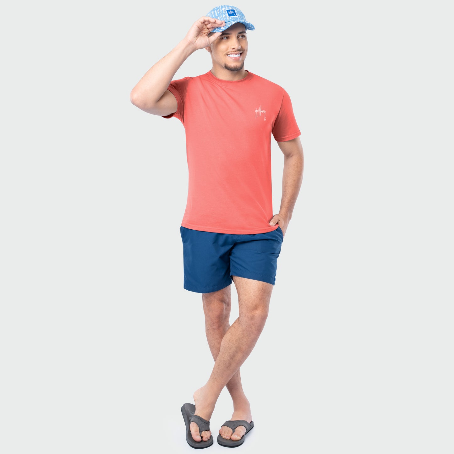 Man wearing a coral t-shirt and blue shorts on a white background