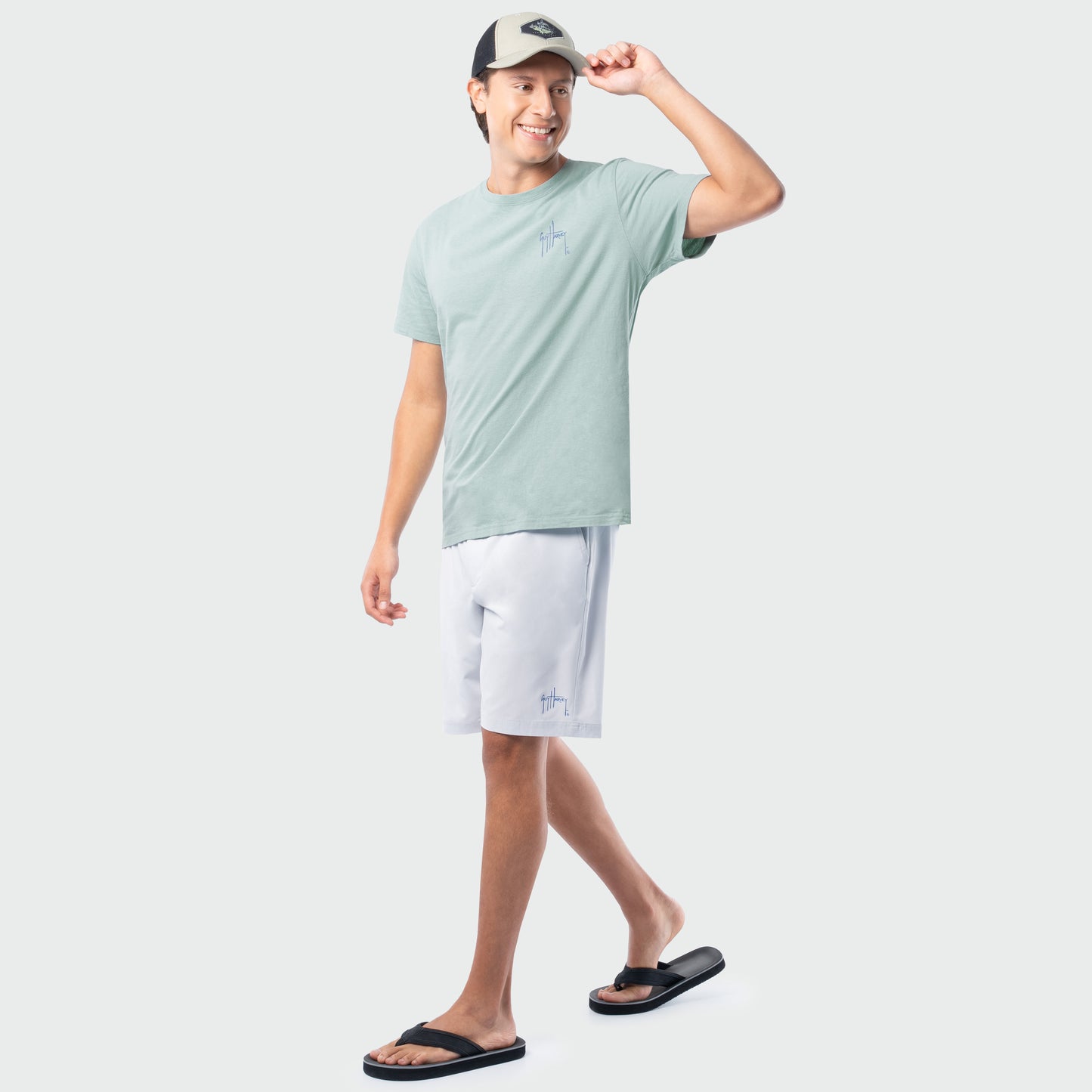 Man wearing a light green t-shirt, white shorts, and black sandals on a white background