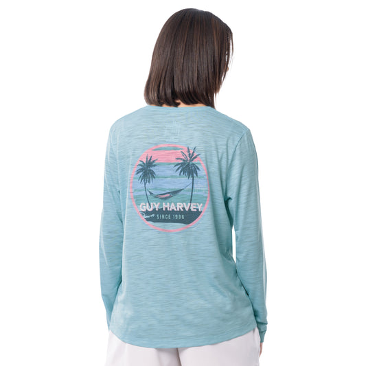 Woman wearing a Guy Harvey long-sleeve shirt with palm tree and a hammock design on a white background