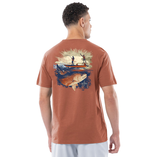 Man wearing a brown t-shirt with a graphic of two people on a boat and a redfish on the back, on a white background.