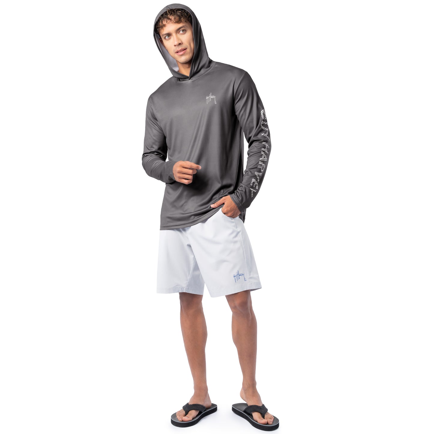 Lifestyle image of model wearing charcoal gray Guy Harvey Men’s Rack Sun Protection Hoodie with hood up and white shorts.