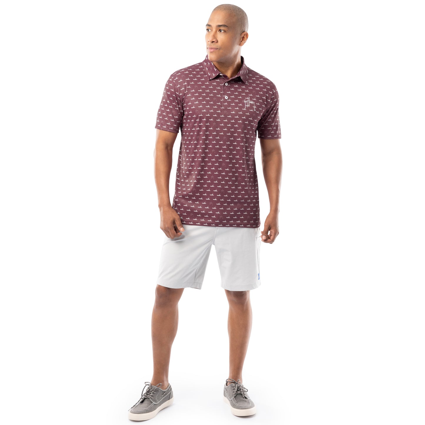 Lifestyle image of model wearing red wine Guy Harvey Men’s Red Fleet Printed Performance Polo with white shorts.