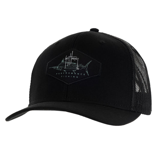 A black trucker hat with a mesh back and a sublimated patch on the crown featuring Guy Harvey's Marlin Sketch drawing and his signature.