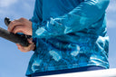 Person wearing a blue textured sun protection shirt holding a fishing rod against a clear sky.