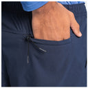 Close-up of a person wearing navy blue technical fishing pants, with one hand tucked into a side pocket. A blue shirt cuff is visible at the top, and a small drawstring with branding hangs from the pocket.