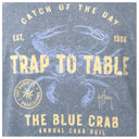 A square graphic print featuring a blue crab illustration with distressed cream text reading 'Catch of the Day,' 'Trap to Table,' 'The Blue Crab,' and 'Annual Crab Boil,' plus 'Est. 1986' and a circular 'Guy Harvey's Provisions' emblem.