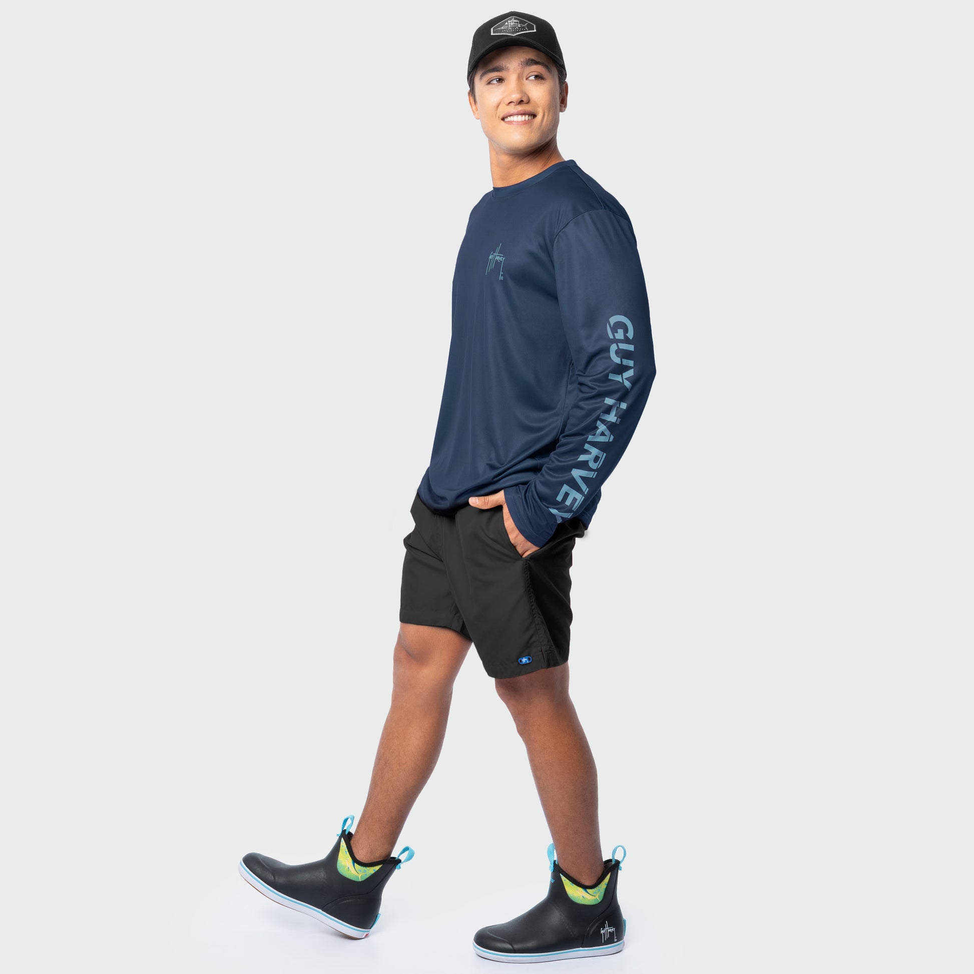 Man wearing a navy long-sleeve shirt with branding, black shorts, and black shoes with yellow accents on a white background.