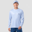 A man wearing a light blue long-sleeve performance shirt with a small dark logo on the left chest and a white baseball cap, standing against a solid light gray background.