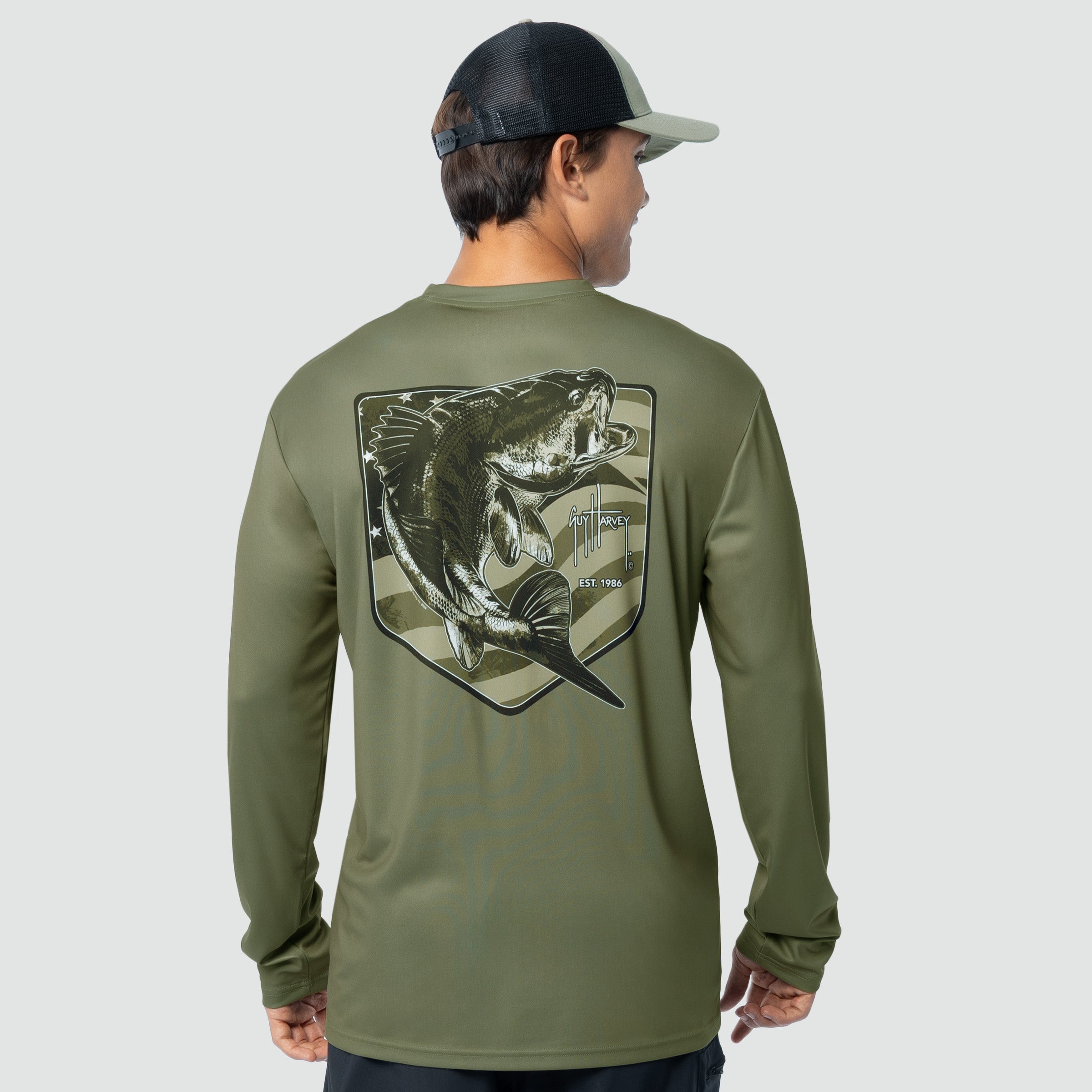 Person wearing a green long-sleeve shirt with a bass fish graphic on the back, standing against a light gray background.