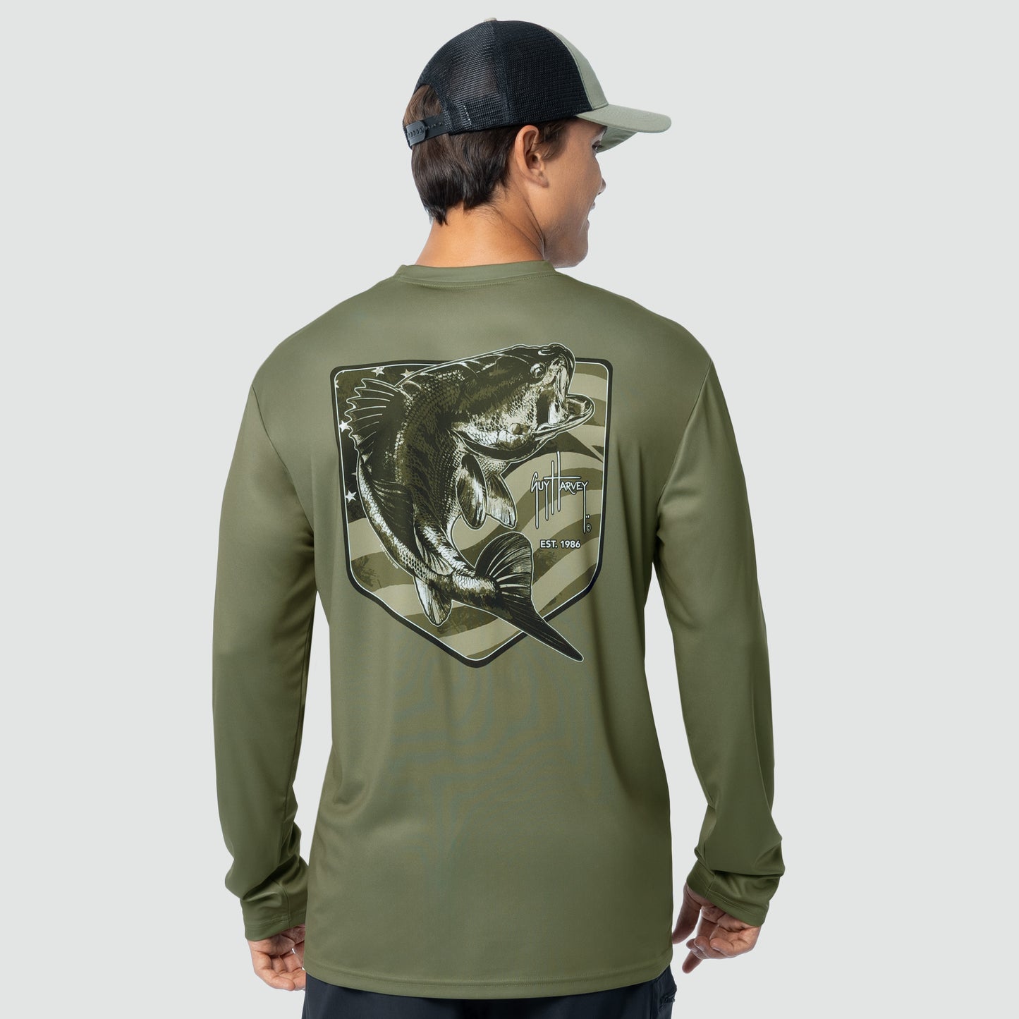 Person wearing a green long-sleeve shirt with a bass fish graphic on the back, standing against a light gray background.