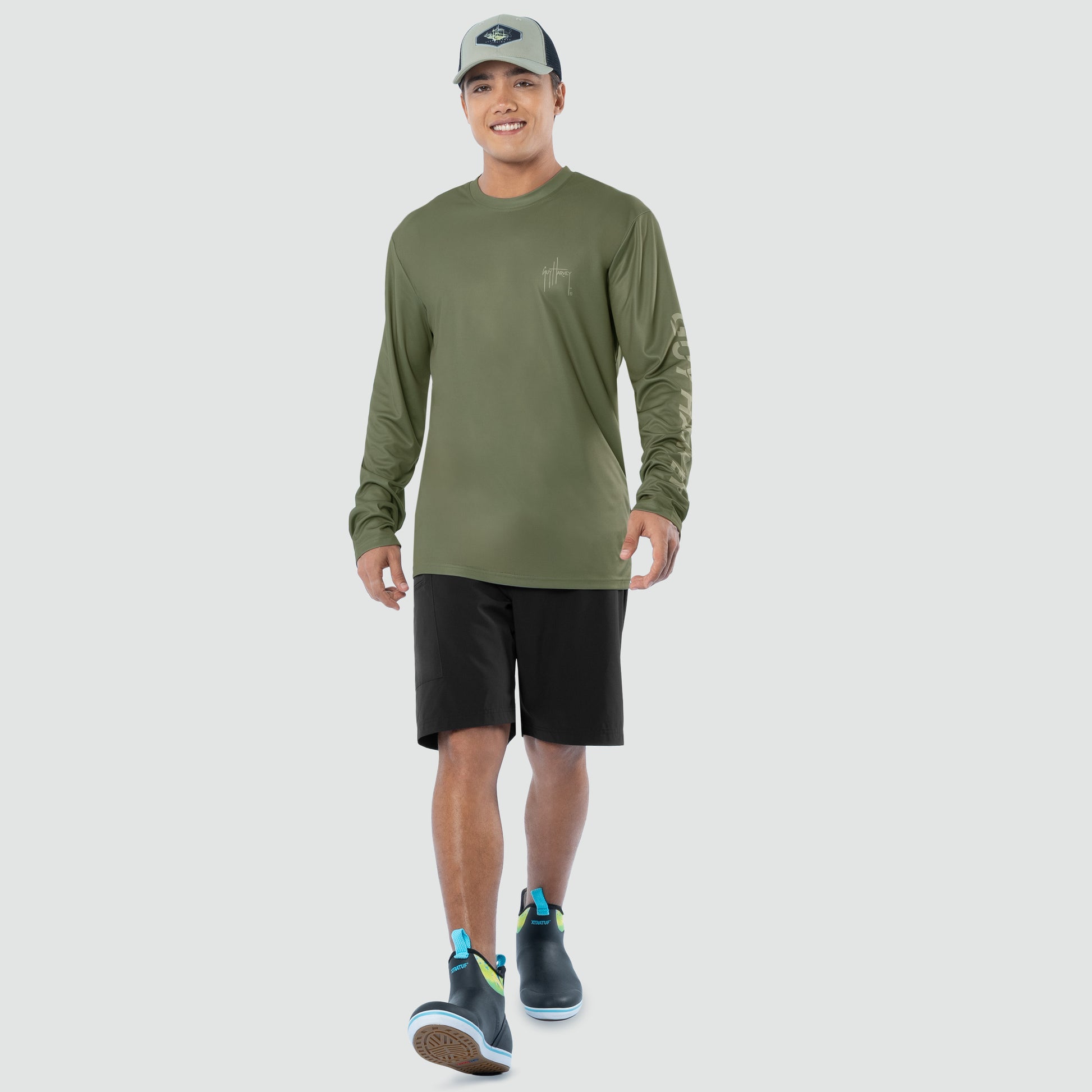 Man wearing a green long-sleeve shirt and black shorts on a light gray background