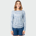 A woman modeling a light blue long-sleeve sun protection top with a subtle heathered texture, paired with navy blue shorts, against a solid light gray background.