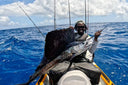 Emmanuel Williams on a jet ski holding a large fish with a blue ocean and sky in the background