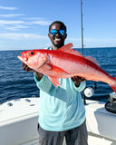 A man holding a fish on a boat smiling with the ocean behind him