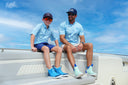 Father and son sitting on a boat under a clear blue sky wearing Guy Harvey button down shirts