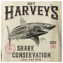 A vintage-style graphic print on a light beige fabric background, featuring a large black-and-white shark illustration with distressed text reading 'GUY HARVEY'S', 'SHARK CONSERVATION', 'SAVE OUR SEAS', and 'ESTD 1986'.