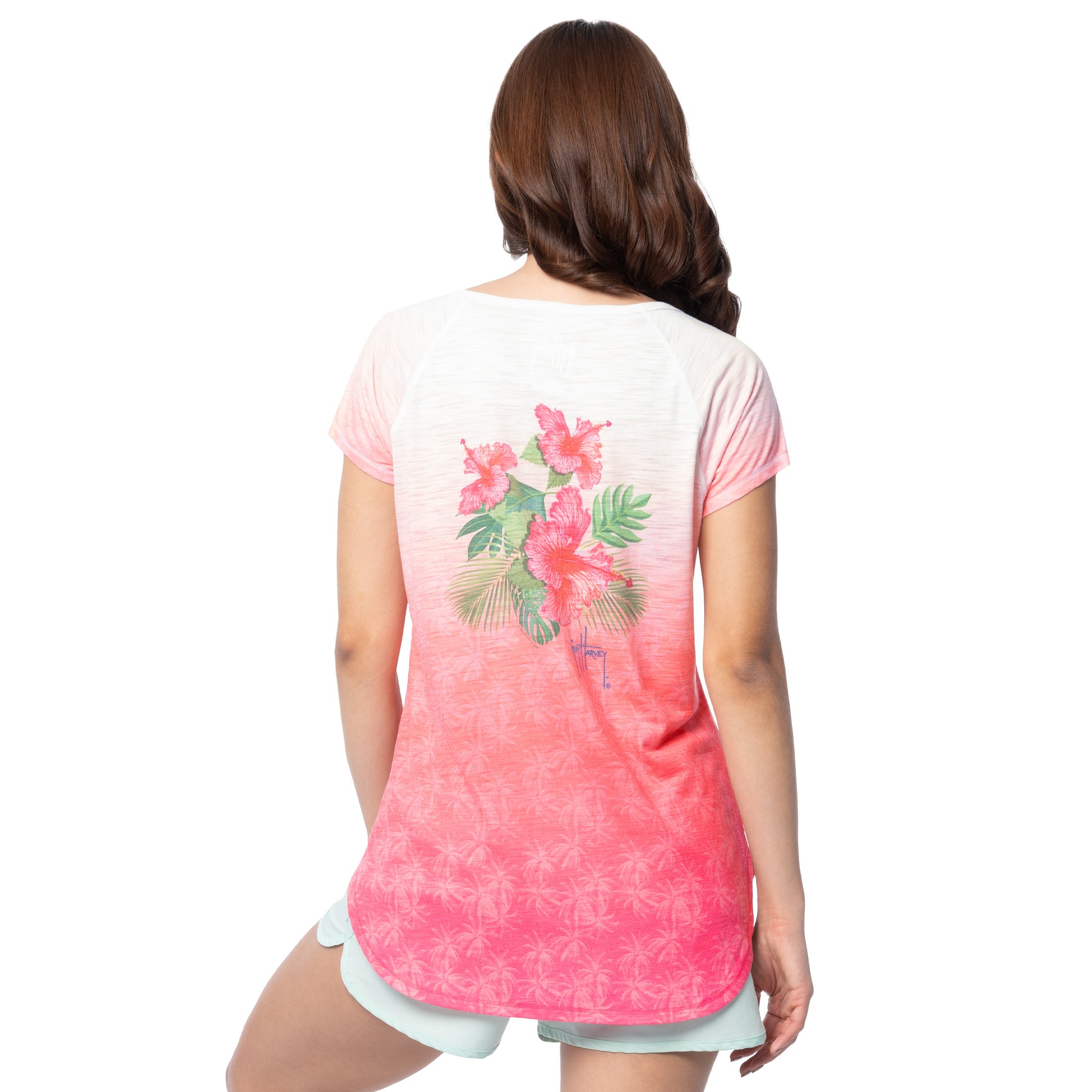Woman wearing a pink and white gradient t-shirt with floral design on the back, on a white background.