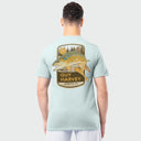 A man wearing a light green Guy Harvey t-shirt featuring a brown trout design on the back against a plain background
