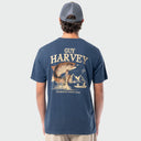 Person wearing a blue Guy Harvey t-shirt with a graphic of a trout fish and mountains on the back.