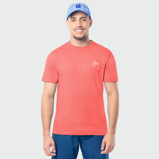 Man wearing a coral t-shirt with a Guy Harvey logo and blue cap on a light gray background