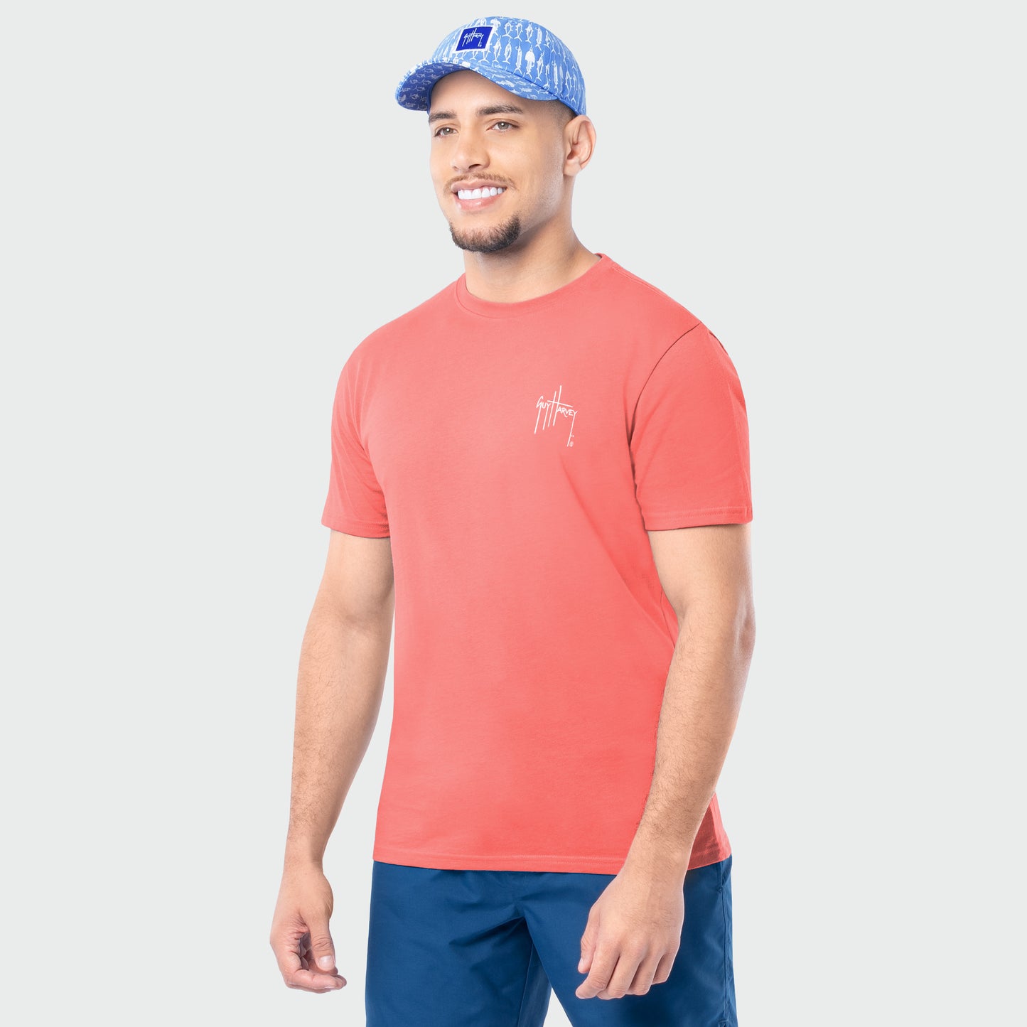 Man wearing a coral t-shirt and blue cap on a light gray background