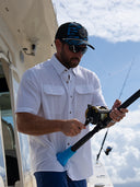 A man wearing a button down perforated shirt by Guy Harvey while fishing offshore