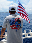 A man wearing a red, white and blue Guy Harvey design of a marlin on grey shirt.