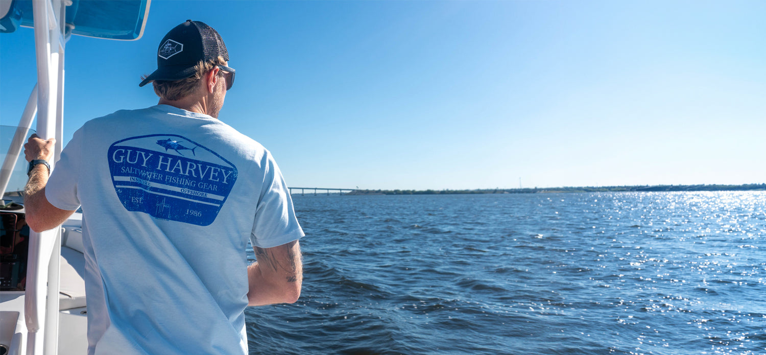 A man wearing a Guy Harvey HarborLite t-shirt on a boat looking out at the ocean.