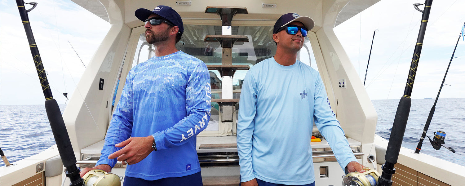 Two men on a boat wearing Guy Harvey Eco Cast Sun Protection Shirts holding fishing rods with a scenic background