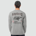 A man viewed from behind wearing a light gray long-sleeve t-shirt with a large shark graphic and 'Guy Harvey's Shark Conservation' text on the back, paired with a dark baseball cap.