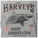 A close-up of a gray graphic t-shirt featuring a black and white shark illustration with distressed text reading 'GUY HARVEY'S' and 'SHARK CONSERVATION'. The design includes a red outline around the main text and a small red seal on the bottom left.