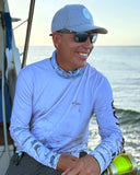 A smiling man on the beach with fishing gear and hat and sunglasses