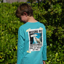 A boy wearing a long sleeve teal Guy Harvey HarborLite tee with a hammerhead shark graphic on the back