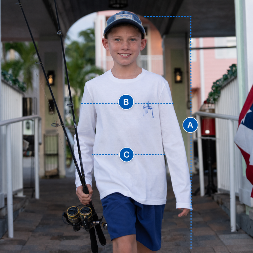 Young boy holding a fishing rod, wearing a white shirt with a logo and blue shorts, standing outdoors.