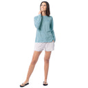 Woman wearing a light blue long-sleeve shirt and white shorts on a white background