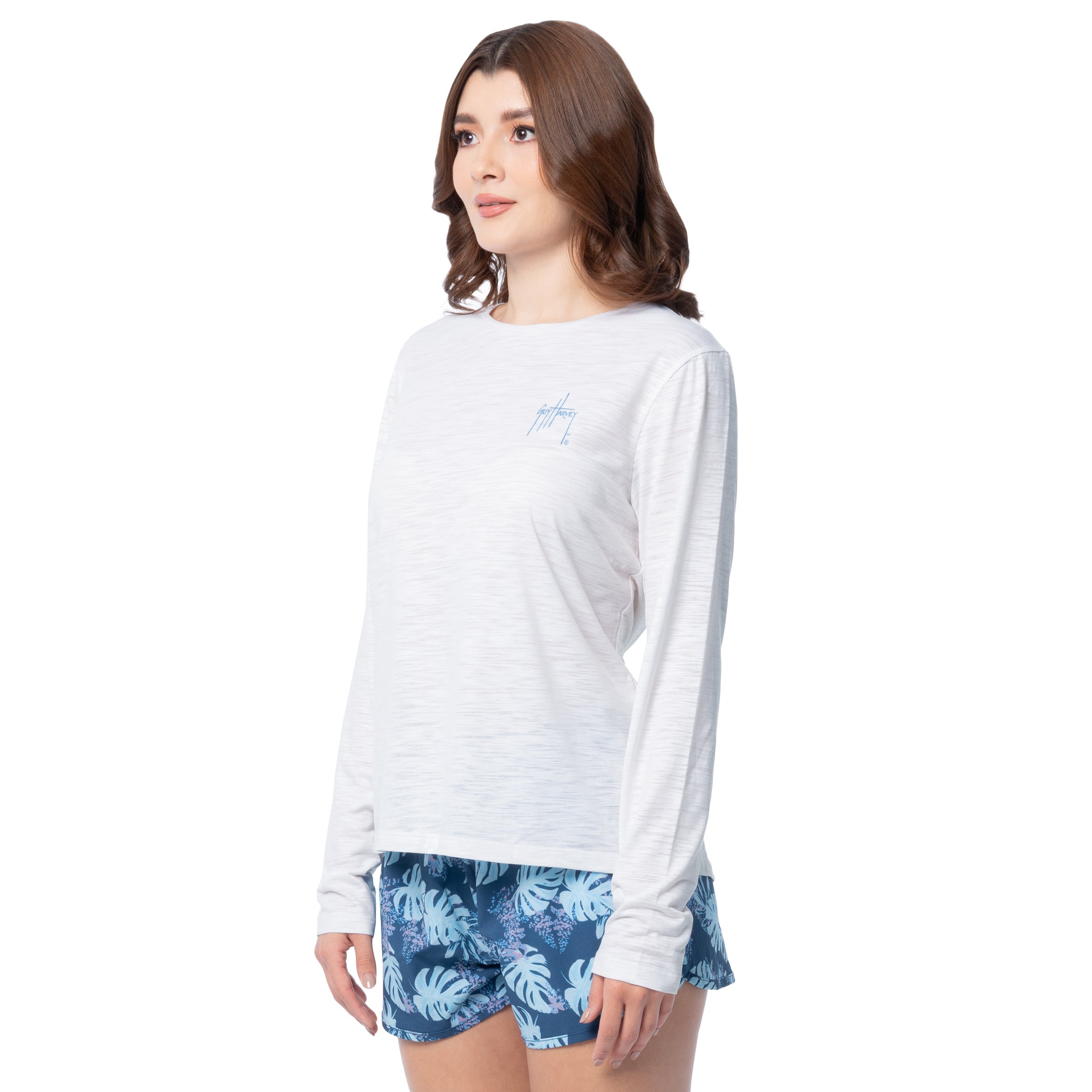 Side view of a woman wearing a white long-sleeve shirt and blue floral shorts on a white background