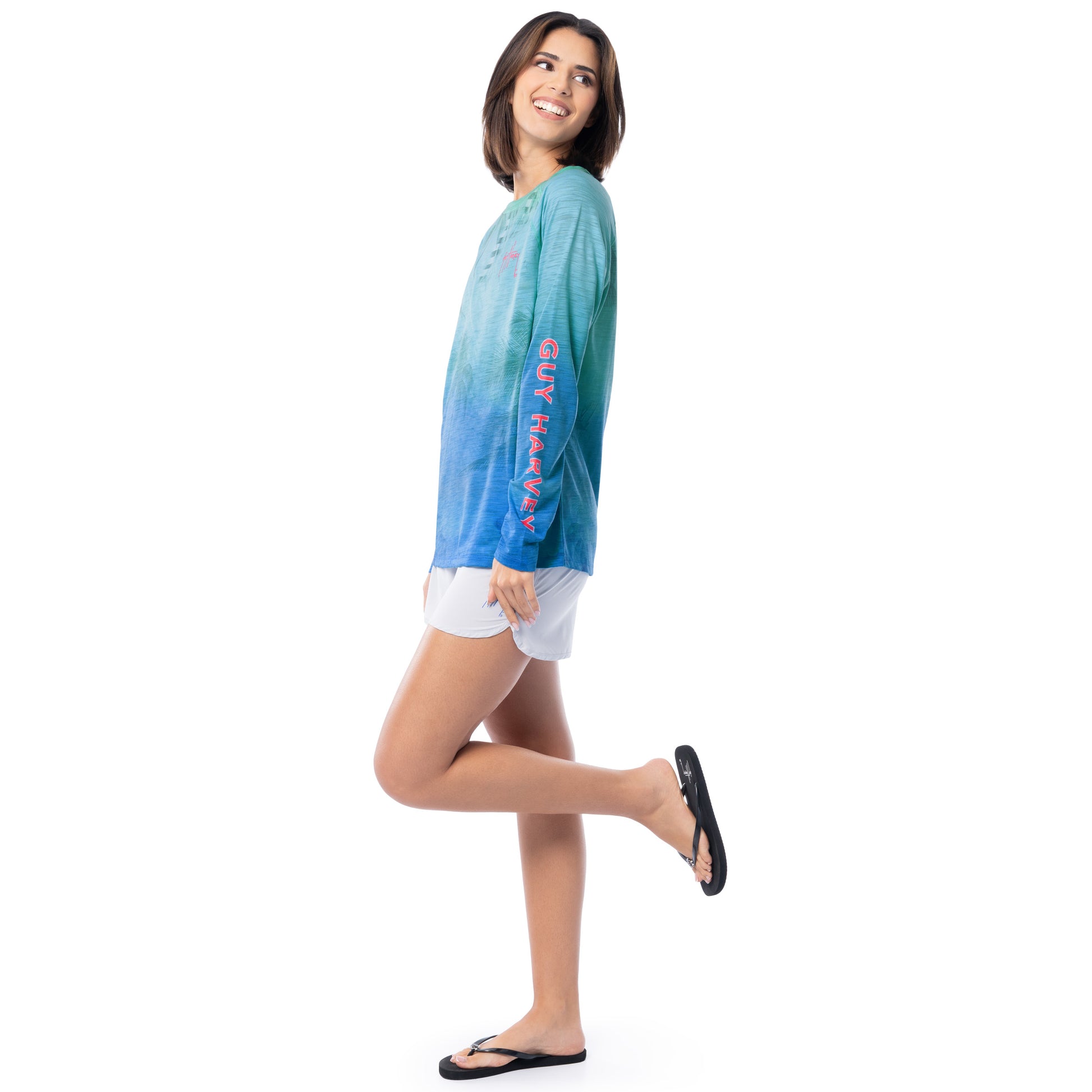 Woman wearing a blue tie-dye shirt with text and white shorts on a white background