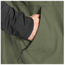 Close-up of a person's hand and sleeve reaching into a side pocket of an olive green lightweight fishing vest.
