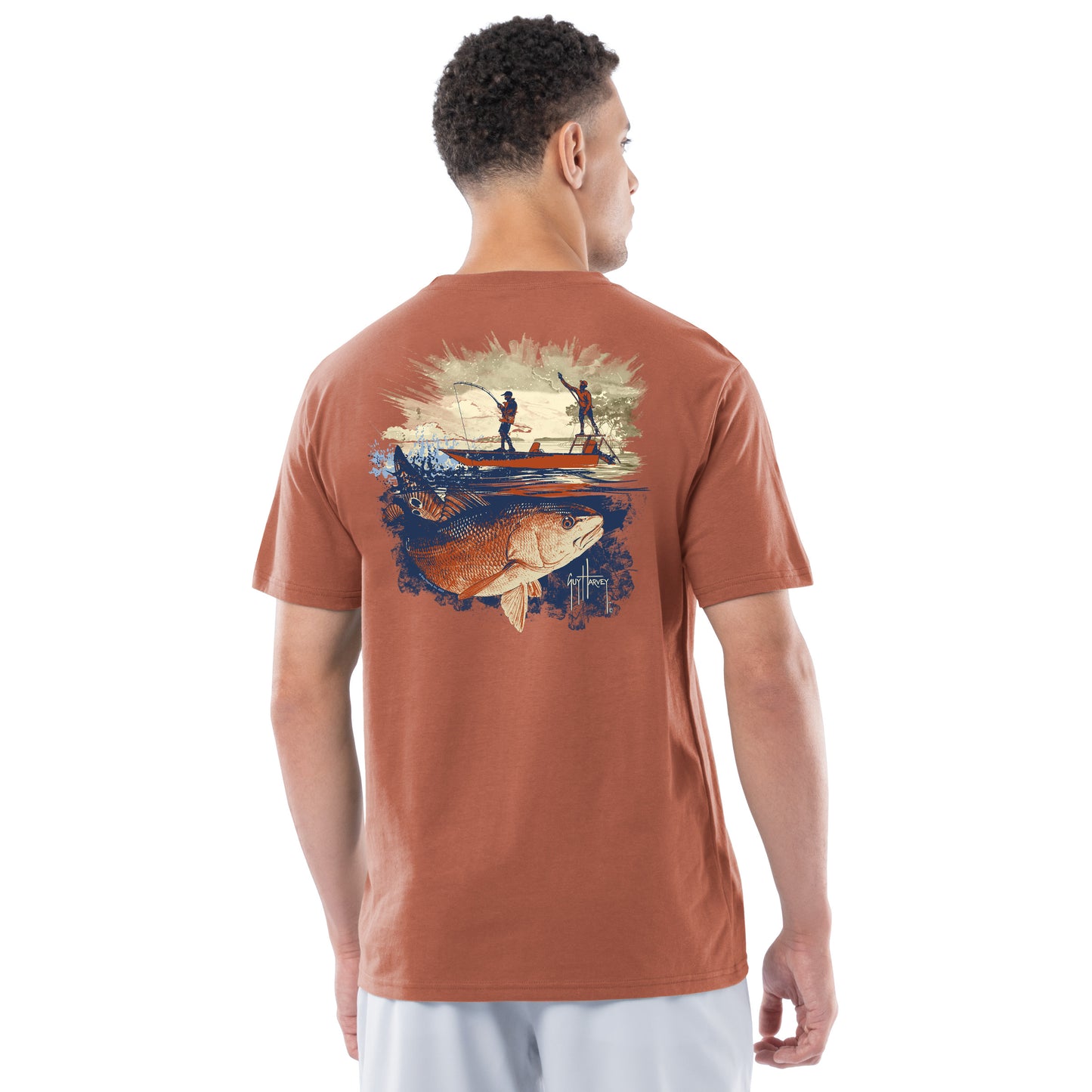 Man wearing a brown t-shirt with a graphic of two people on a boat and a redfish on the back, on a white background.