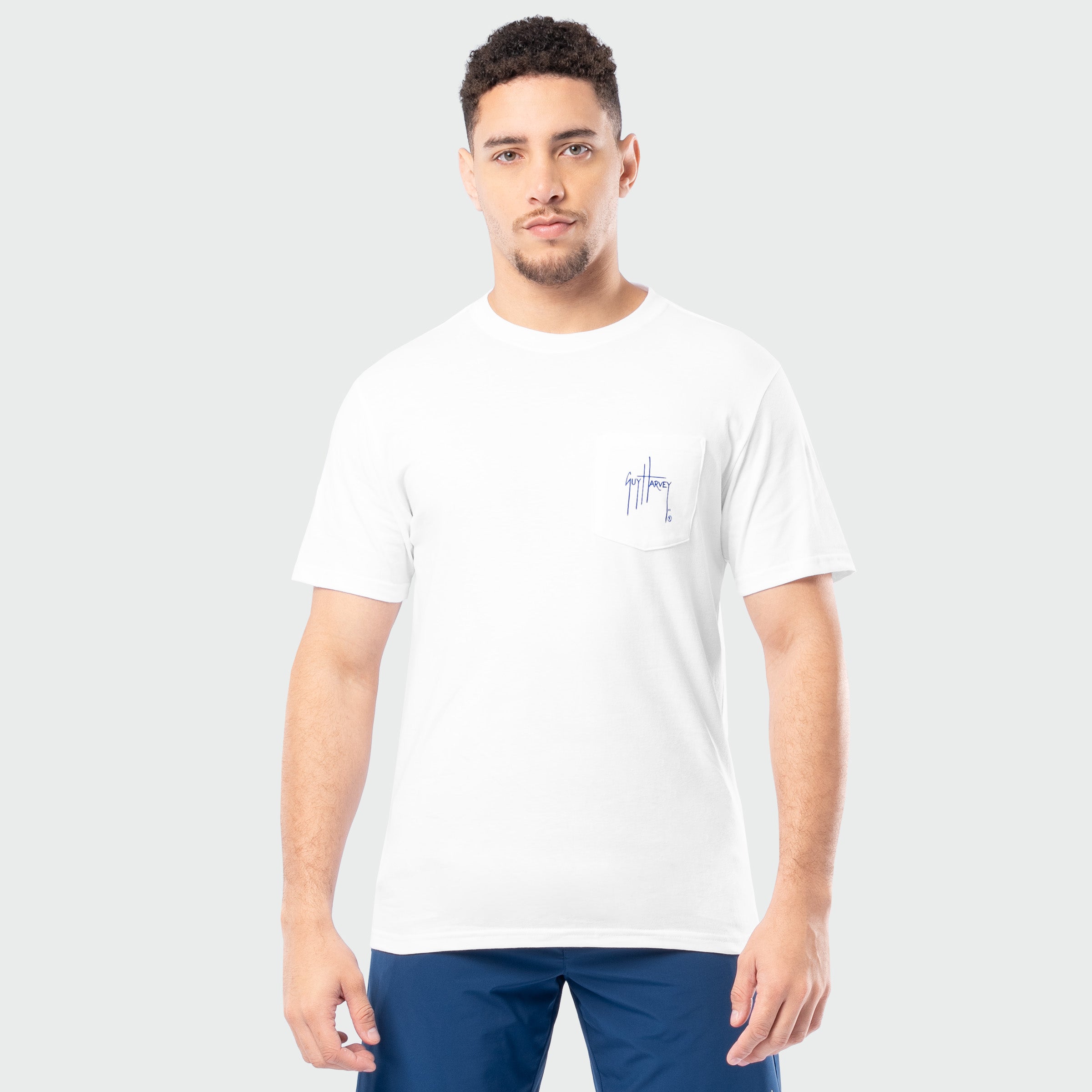 Man wearing a white t-shirt with a small Guy Harvey logo on a plain background