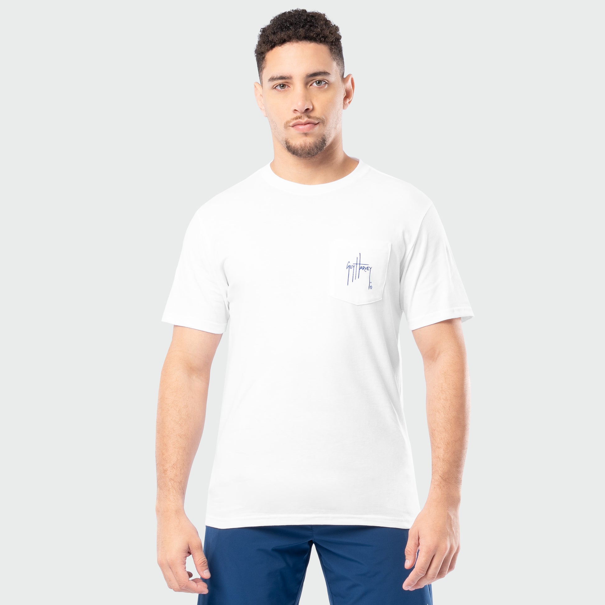 Man wearing a white t-shirt with a small Guy Harvey logo on a plain background