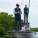 A man wearing Angler Edge fishing pant in navy blue while casting a rod on a boat.