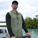 A man driving a boat wearing a black Guy Harvey Marlin Air sun protection top and Olive green Angler Edge Vest.