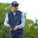 A man wearing a navy Guy Harvey Angler Edge Vest over a blue camo Marlin Air Sun protection hood while fishing.