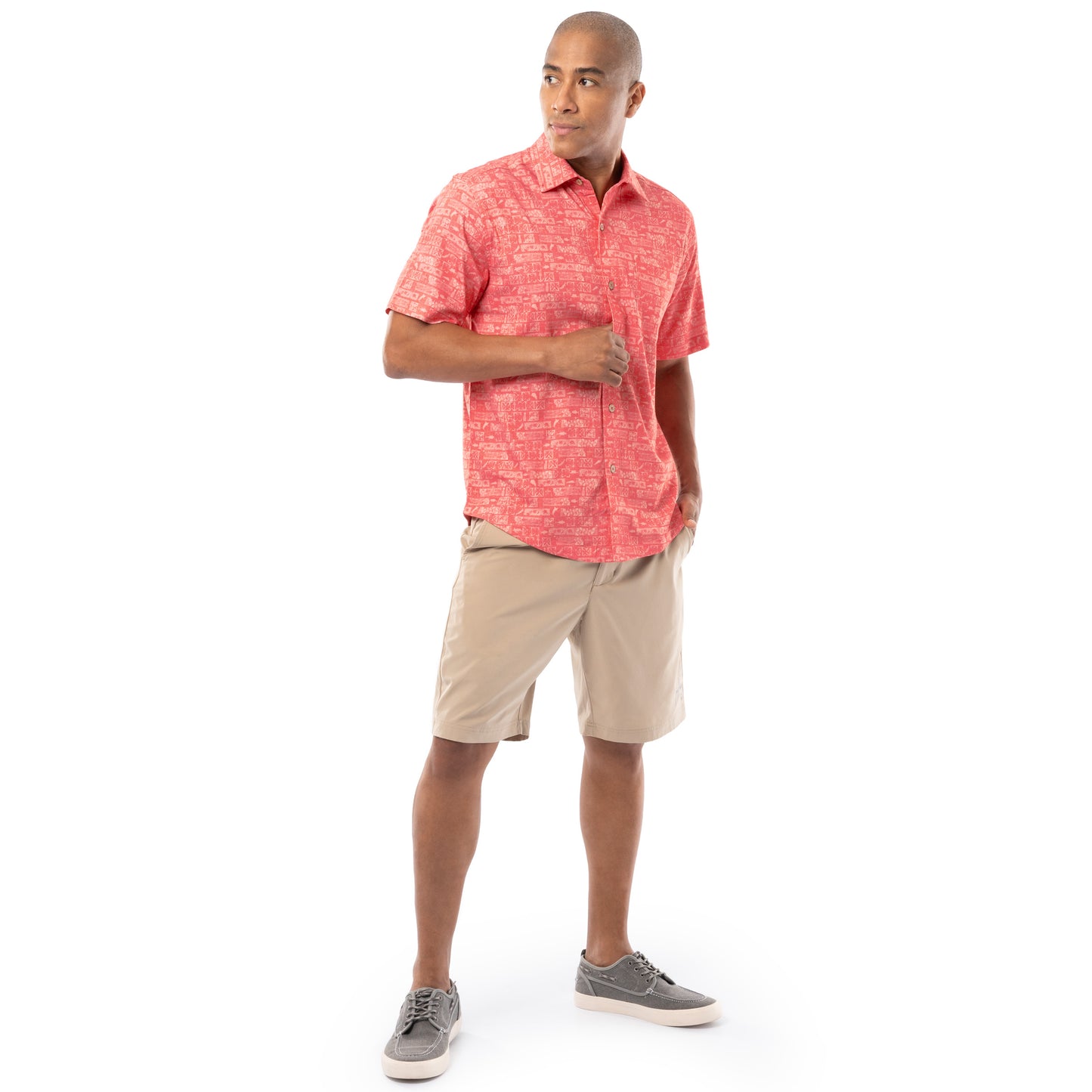 Lifestyle image of model wearing coral red Guy Harvey Men’s Aztec Printed Resort Shirt with khaki shorts.