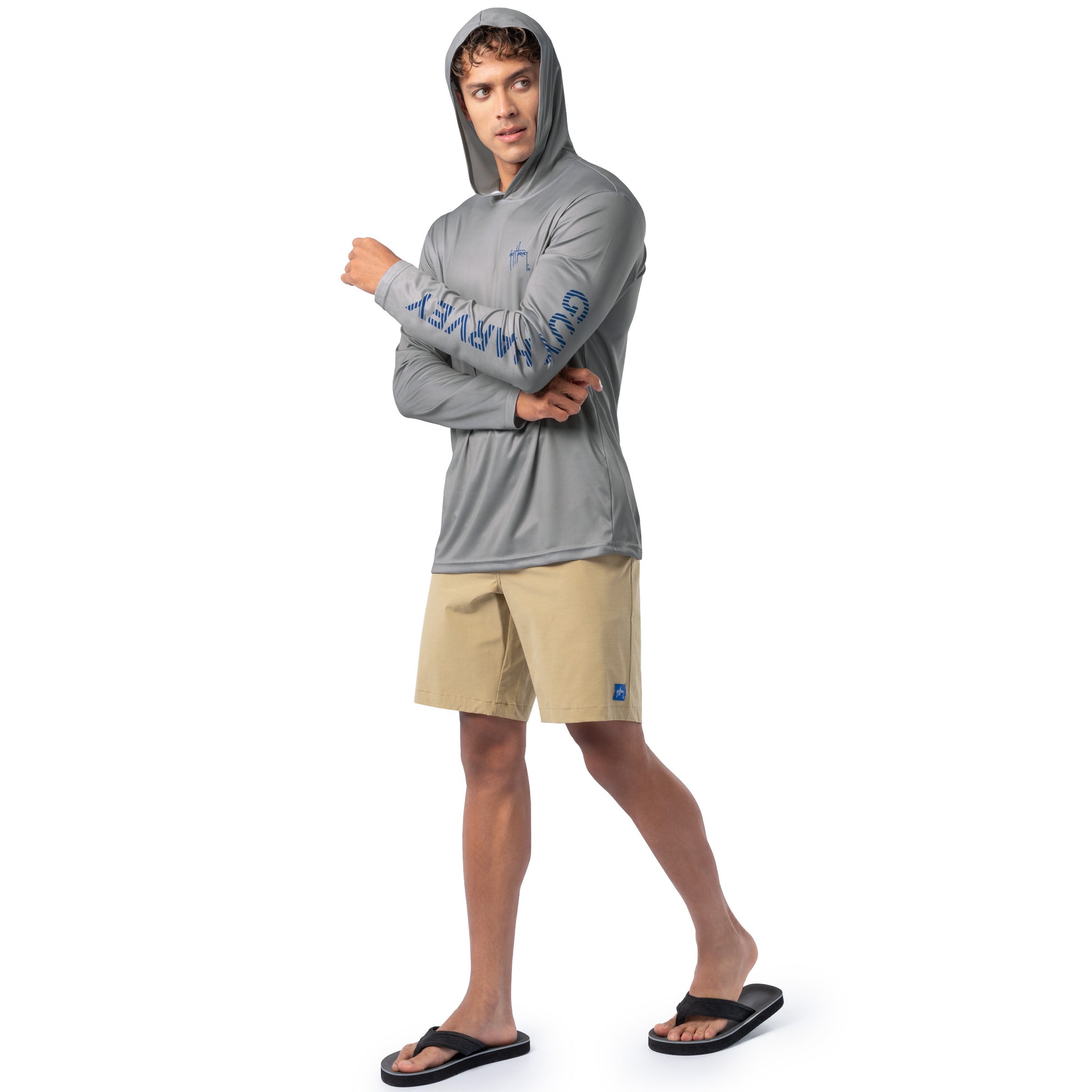 Lifestyle image of model wearing light gray Guy Harvey Men’s Bass Diamond Hoodie with hood up and tan shorts.