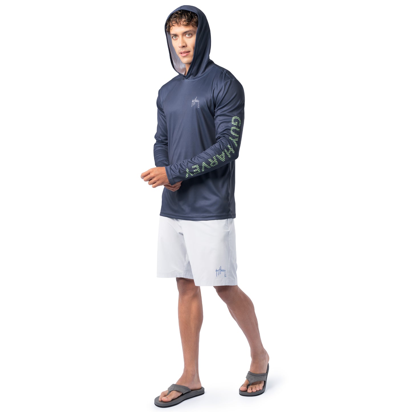 Lifestyle image of model wearing navy blue Guy Harvey Men’s Billfish Slam Sun Protection Hoodie with hood up and white shorts.