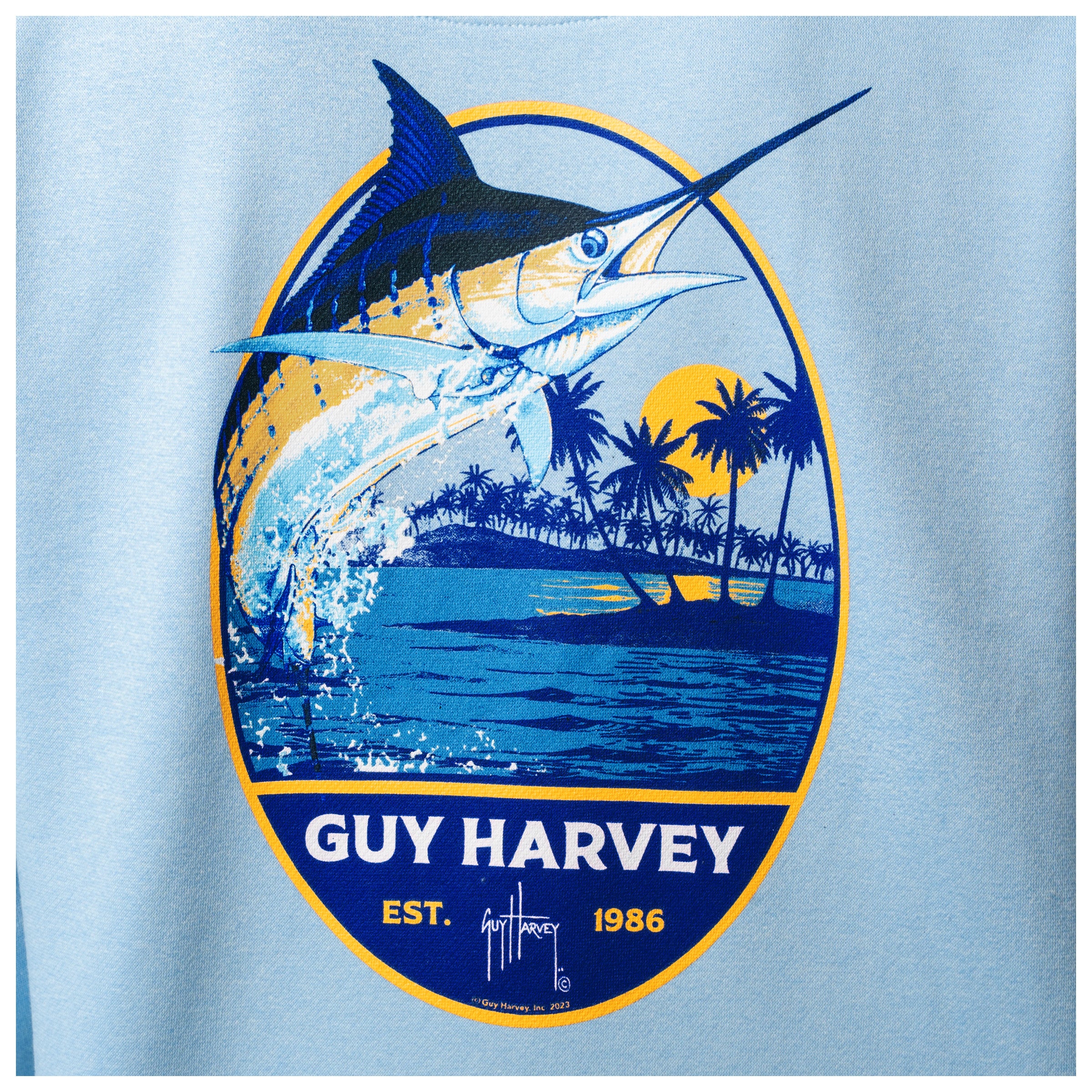Close-up of the marlin and palm tree artwork printed on the back of a light blue Guy Harvey fishing fleece hoodie.
