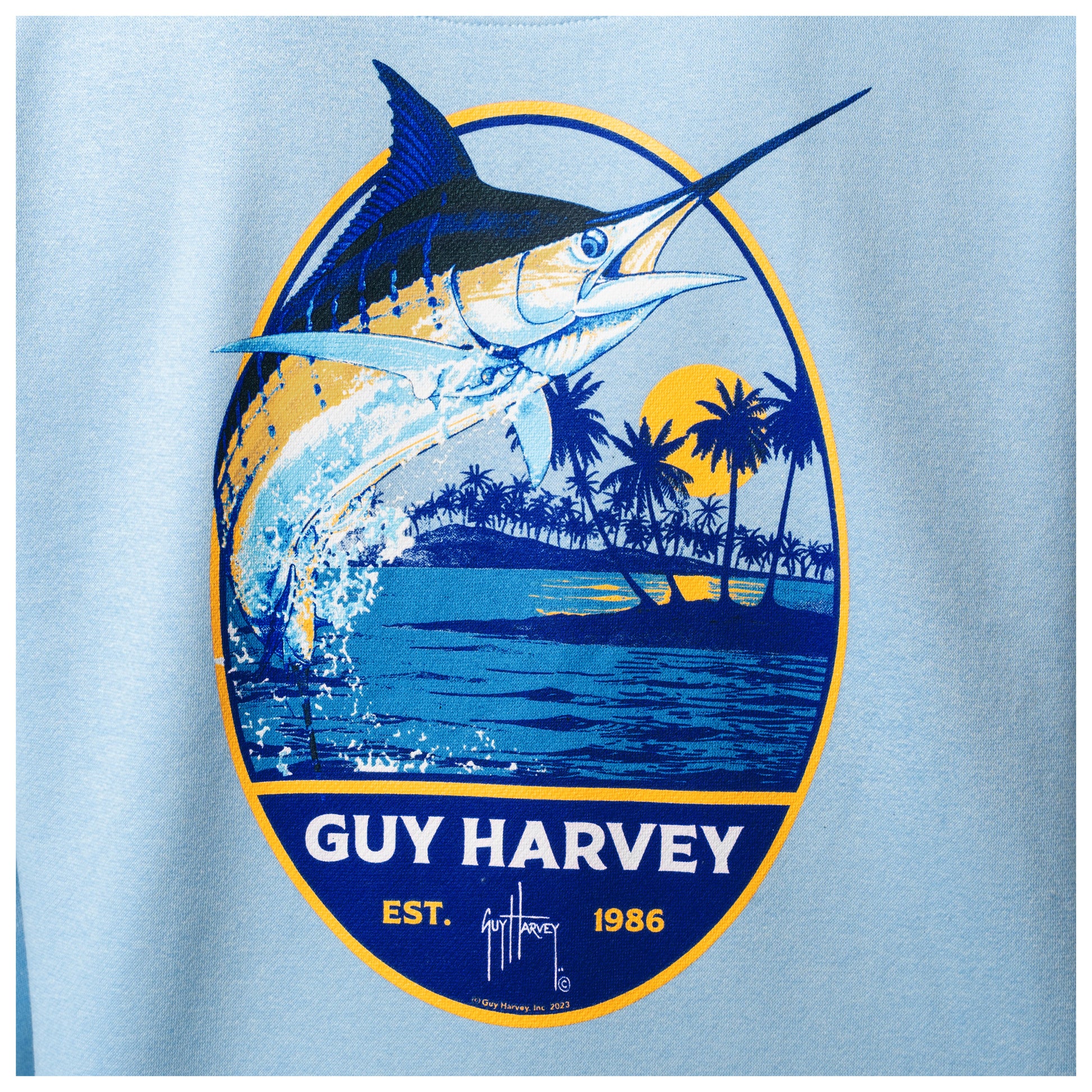 Close-up of the marlin and palm tree artwork printed on the back of a light blue Guy Harvey fishing fleece hoodie.