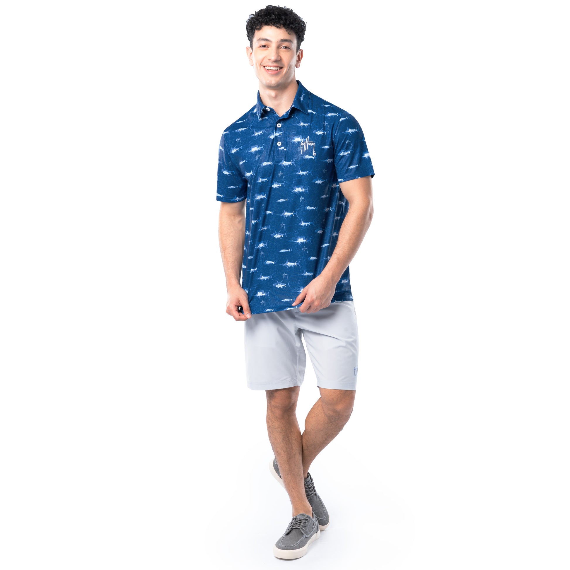 Lifestyle image of model wearing ocean blue Guy Harvey Men’s Double Vision Printed Performance Polo with gray shorts.